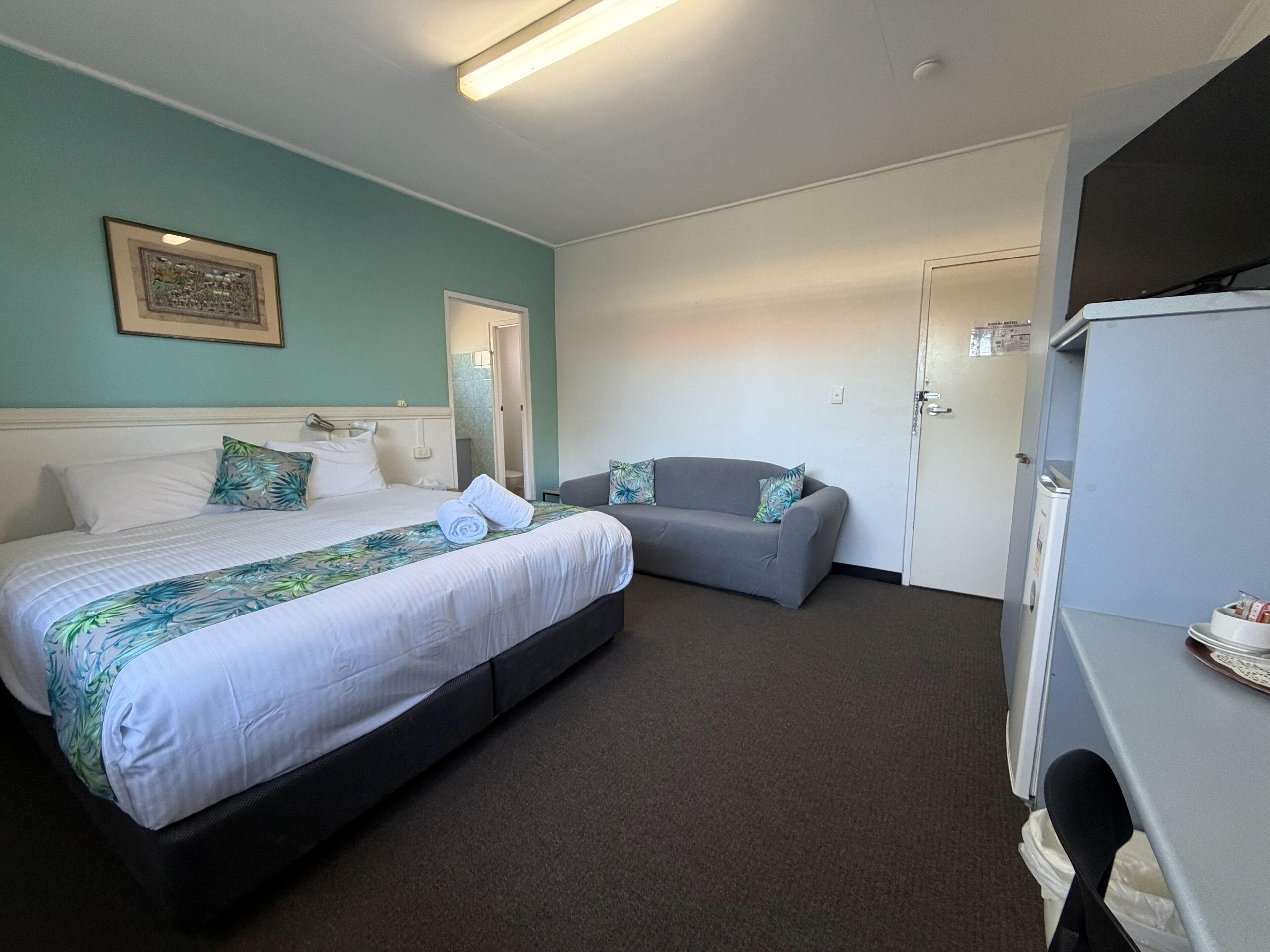 A hotel room with a bed, a sofa, a desk, and a door.