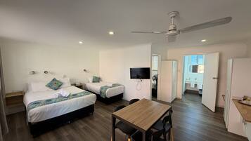 A hotel room with two beds, a dining table, a TV, and a ceiling fan.
