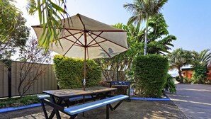 An outdoor patio with a picnic table, a grill, and a large umbrella providing shade.