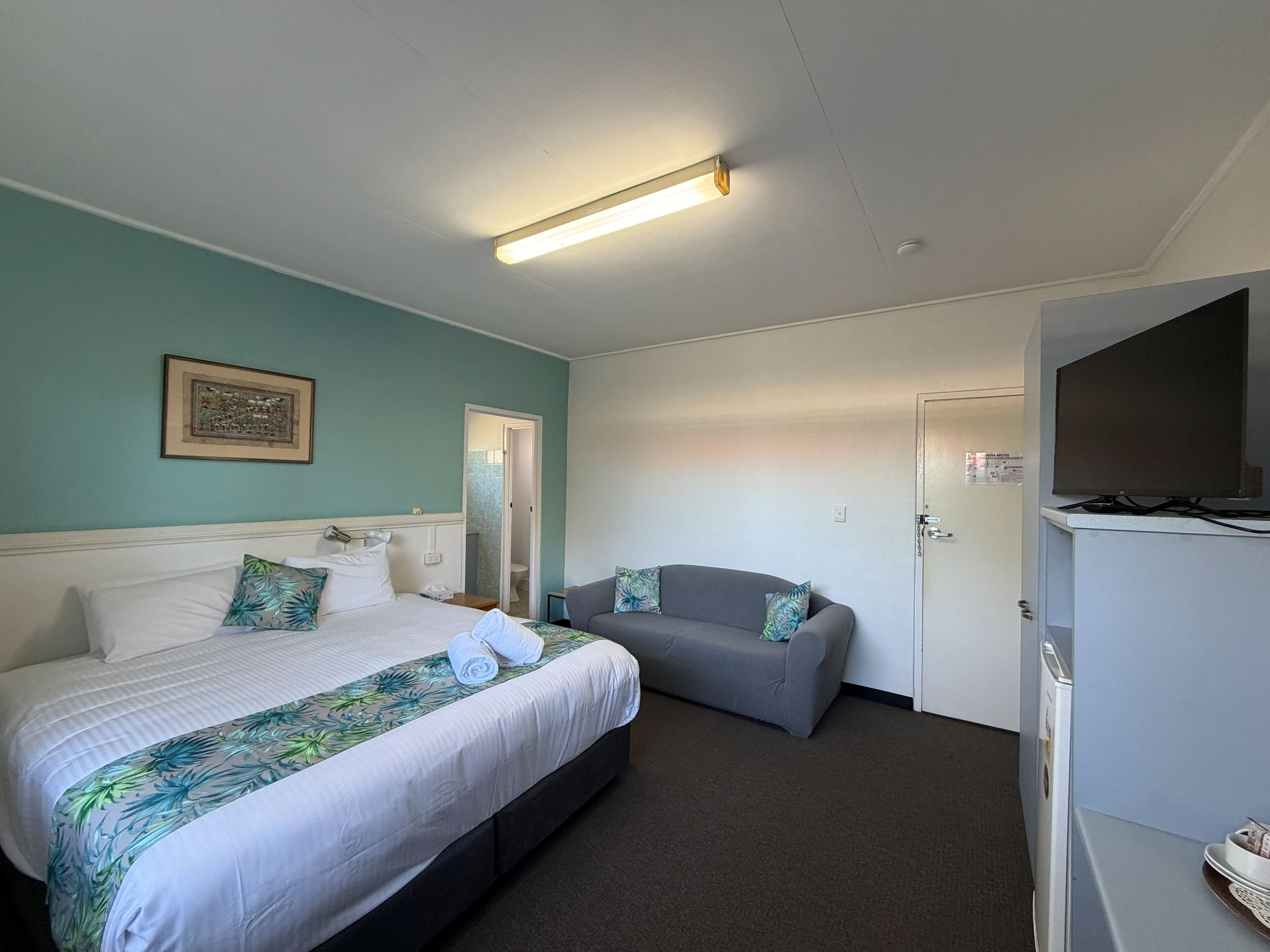 A hotel room with a bed, a sofa, a television, and a door.