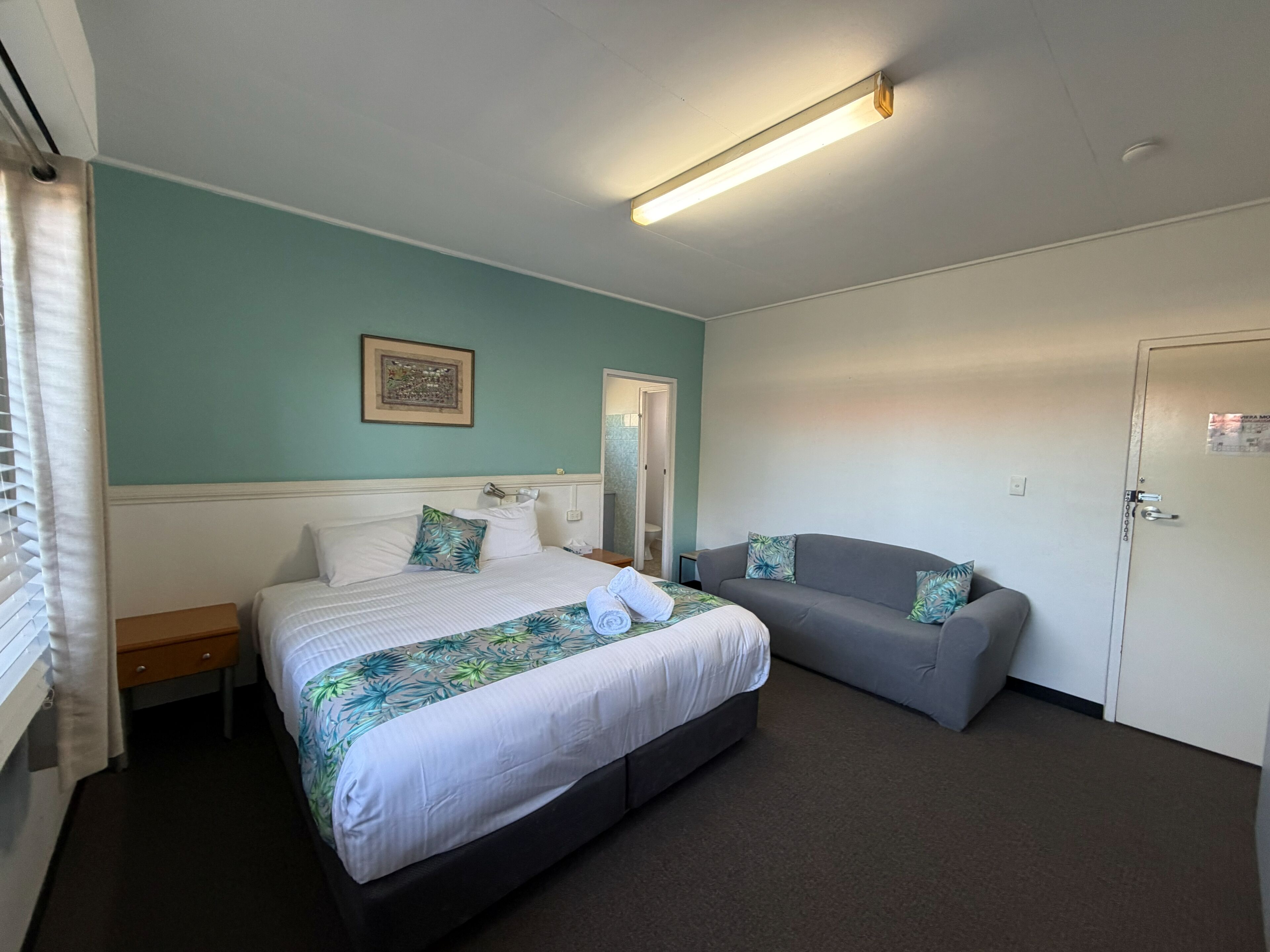 A bedroom with a bed, a sofa, a door, and a framed picture on the wall.