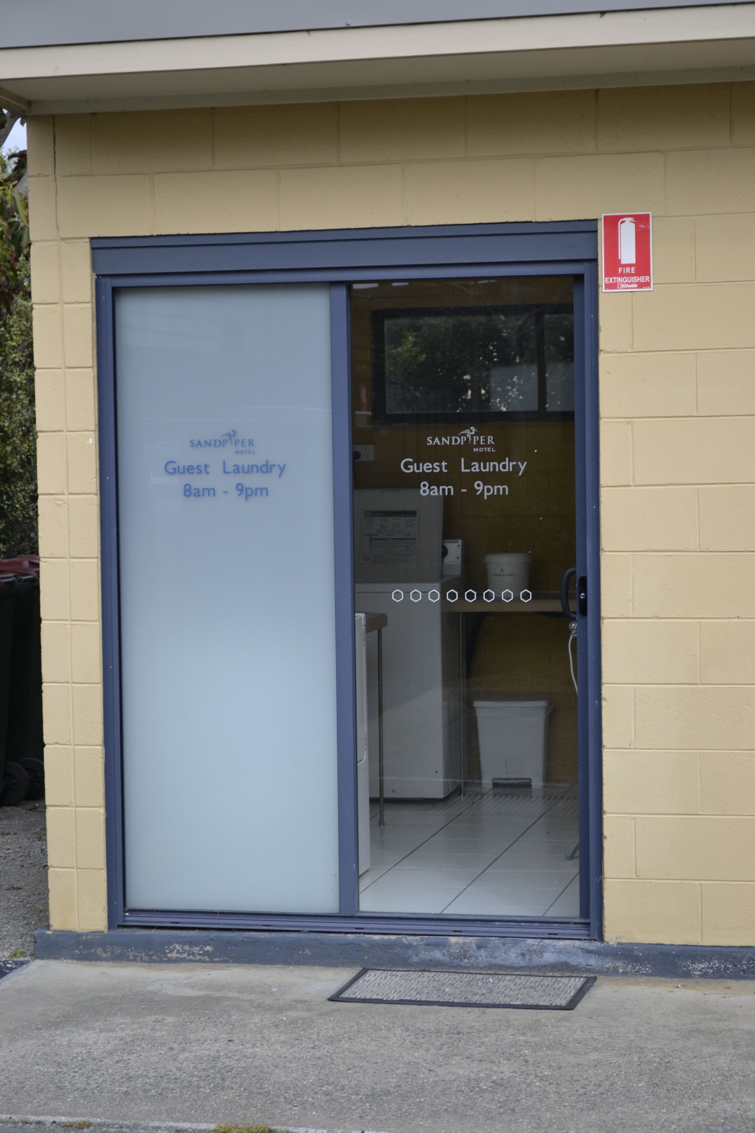 Un espace buanderie à la disposition des clients, avec un panneau indiquant qu’il est ouvert de 8h à 21h.