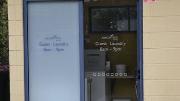 Un espace buanderie à la disposition des clients, avec un panneau indiquant qu’il est ouvert de 8h à 21h.
