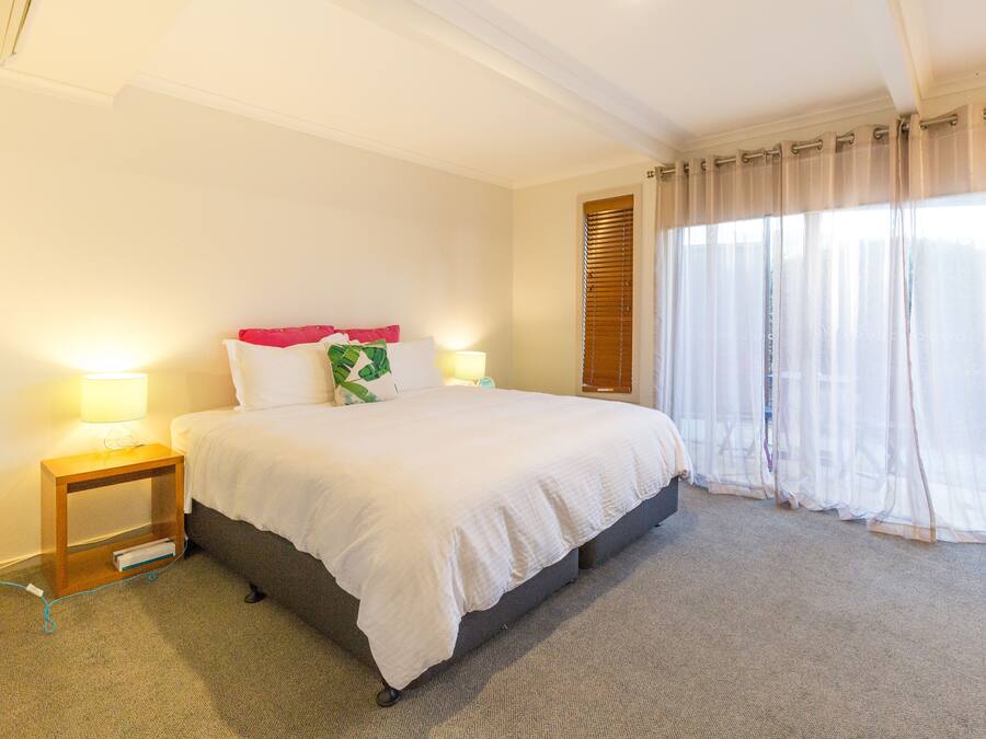 Una habitación de hotel con una cama grande, lámparas de noche, una mesita de madera y cortinas translúcidas.