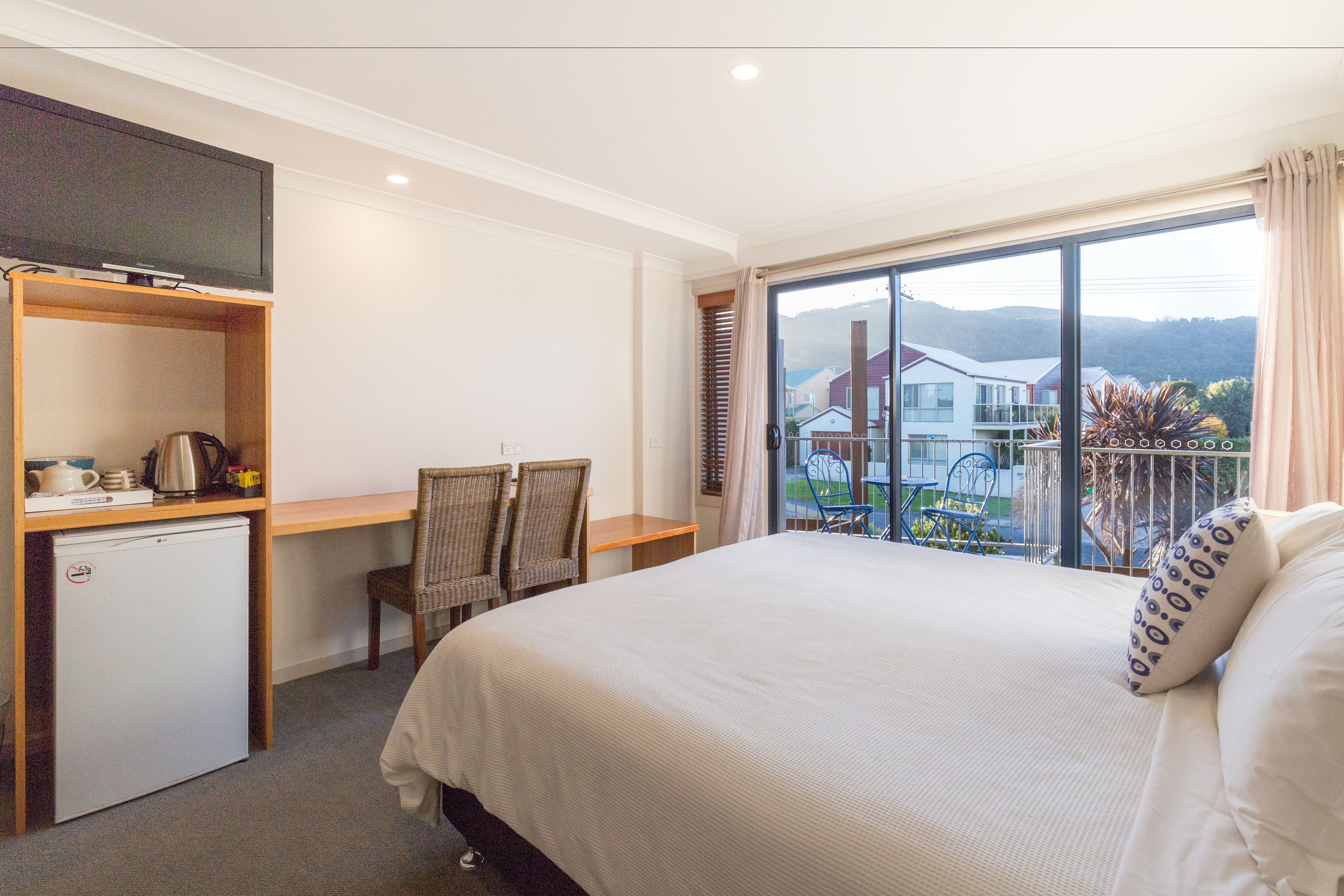 Een hotelkamer met een bed, een bureau met stoelen, een televisie en een kleine koelkast.