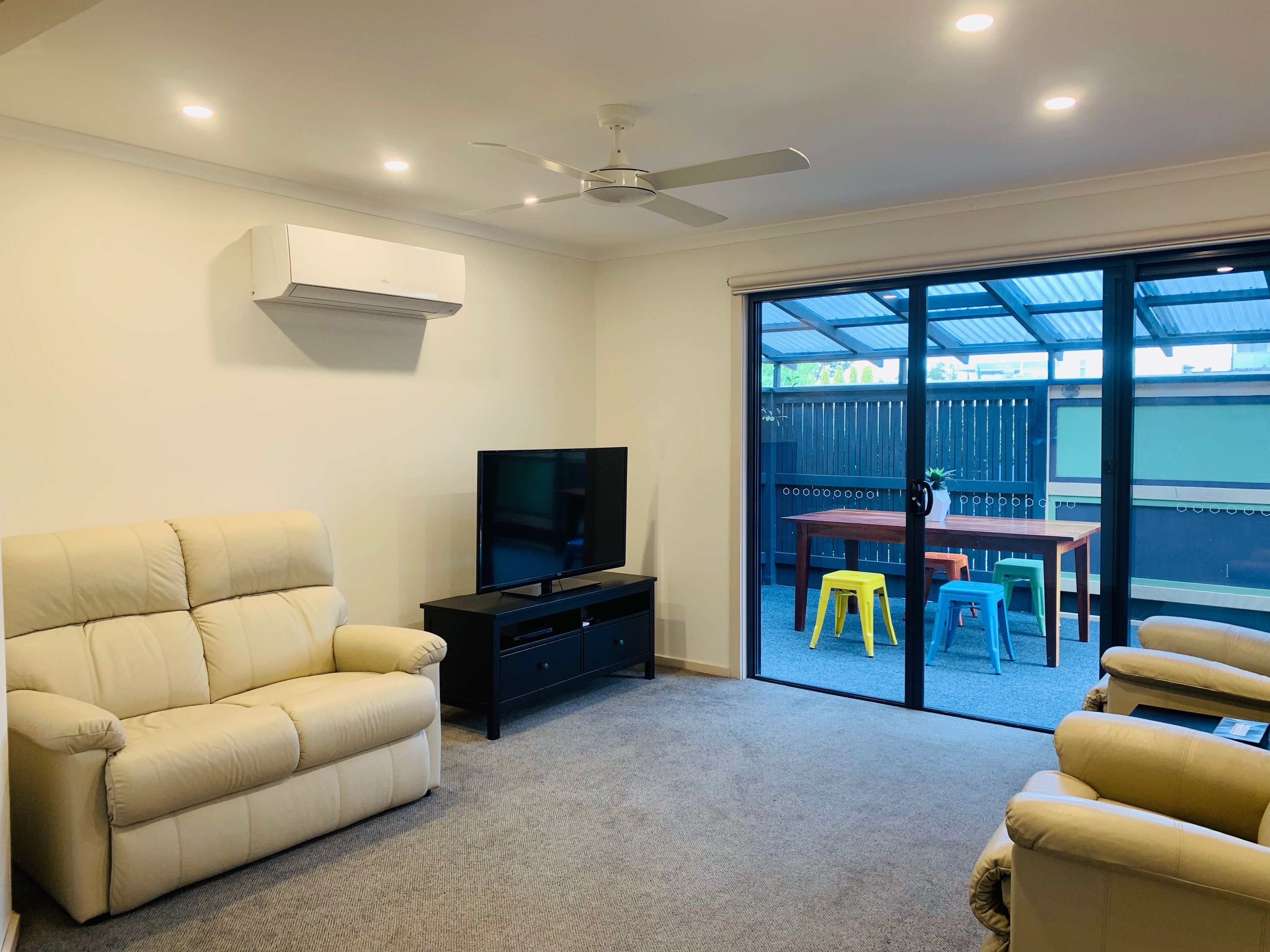 A living room with a beige sofa, a TV on a black stand, and a ceiling fan.