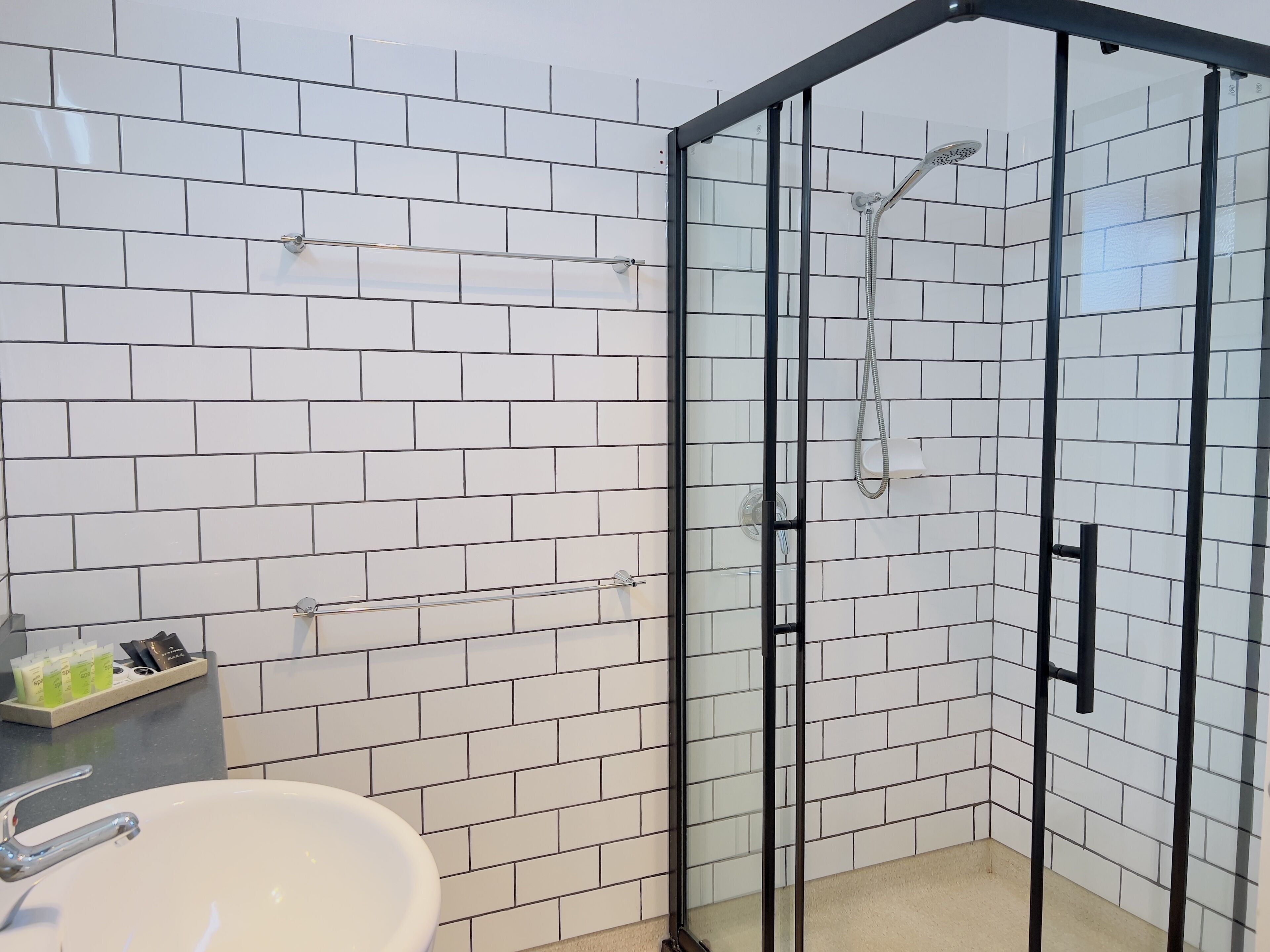 Een badkamer met witte betegeling, een douche met glazen wand, een wastafel en een zeepdispenser op het aanrecht.