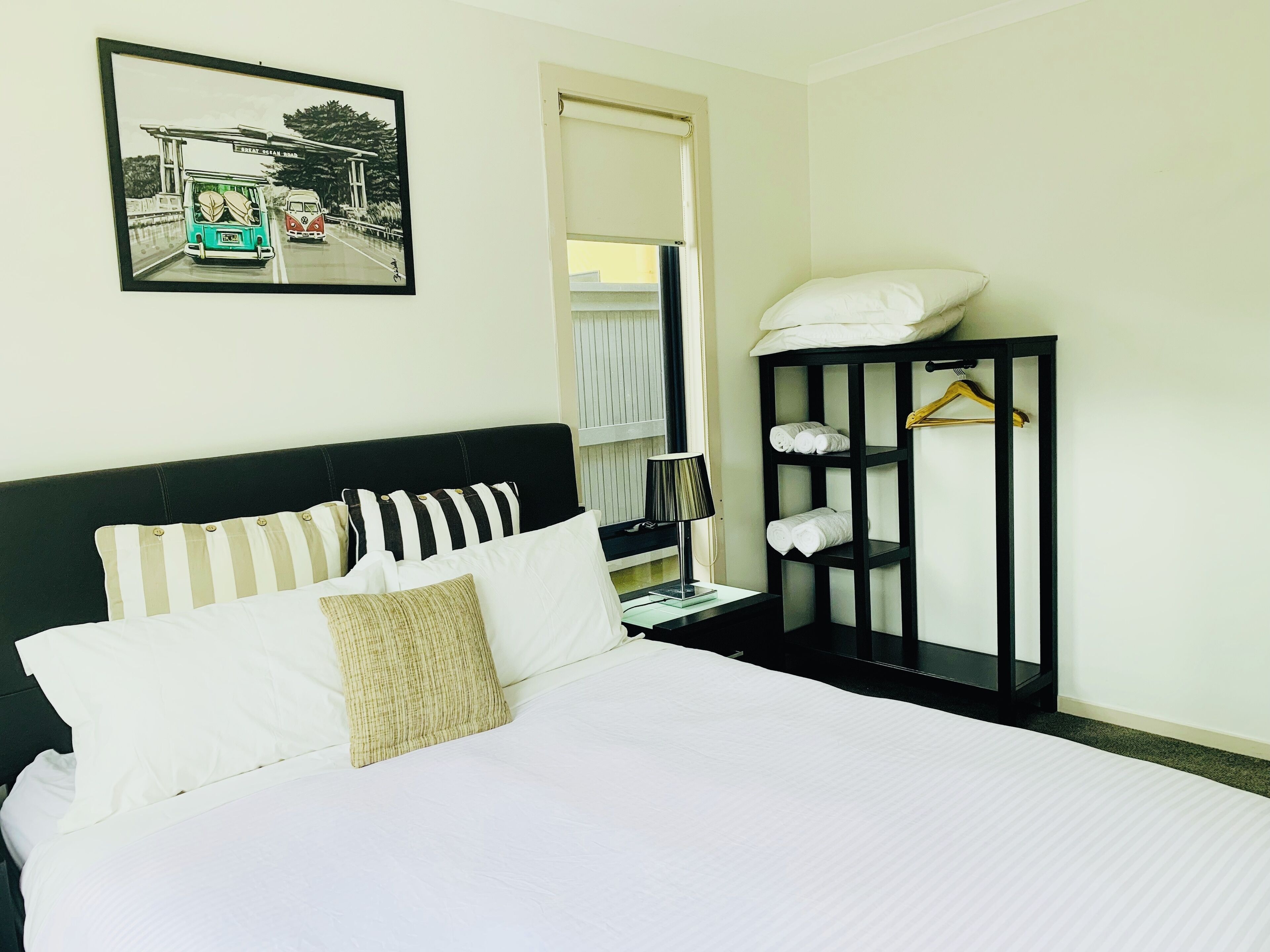 Ein Hotelzimmer mit einem Bett, einem schwarzen Kopfteil, einem Nachttisch mit Lampe, einem Kleiderschrank und einem gerahmten Bild an der Wand.