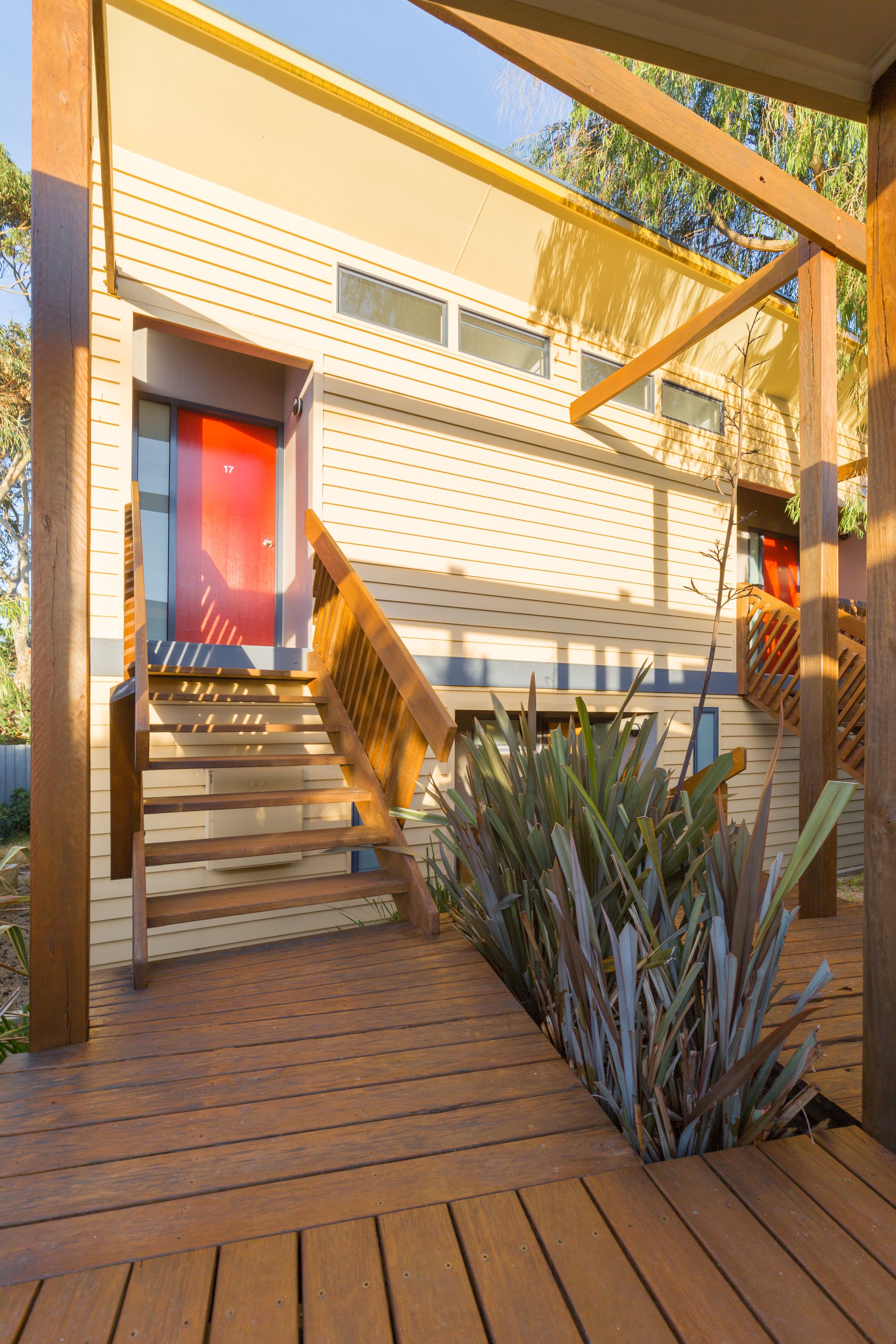 Una terraza de madera con una escalera que lleva a un edificio con una puerta roja.