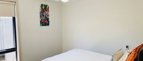 Un dormitorio con una cama, ventilador de techo, ventana y una obra de arte colgada en la pared.