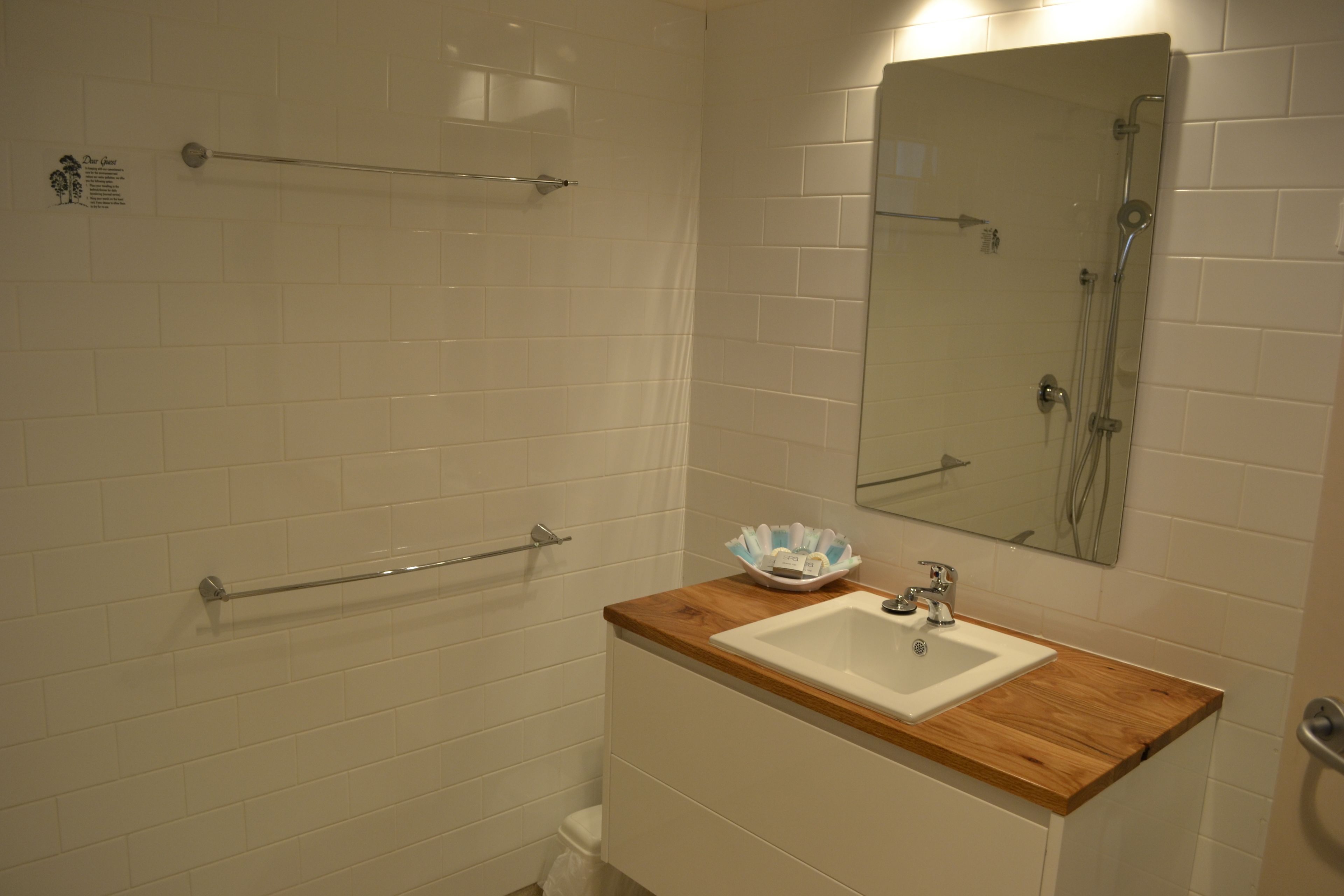 Une salle de bain avec des carreaux blancs, un plan de toilette en bois, un lavabo, un miroir et un espace douche.