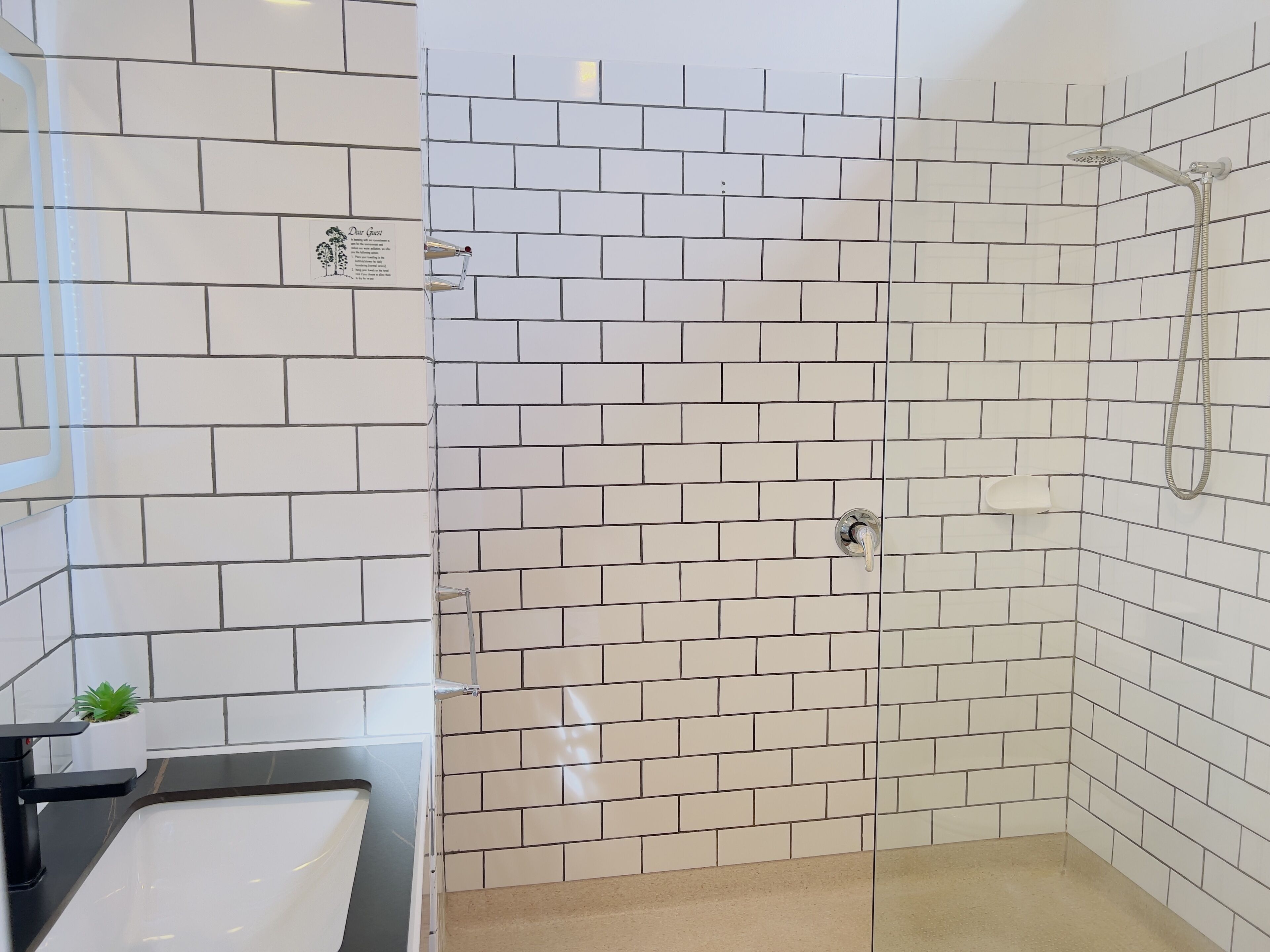 Ein Badezimmer mit weißen Fliesen, einer Dusche mit Duschbrausehandstück und einem Waschbecken mit Spiegel.