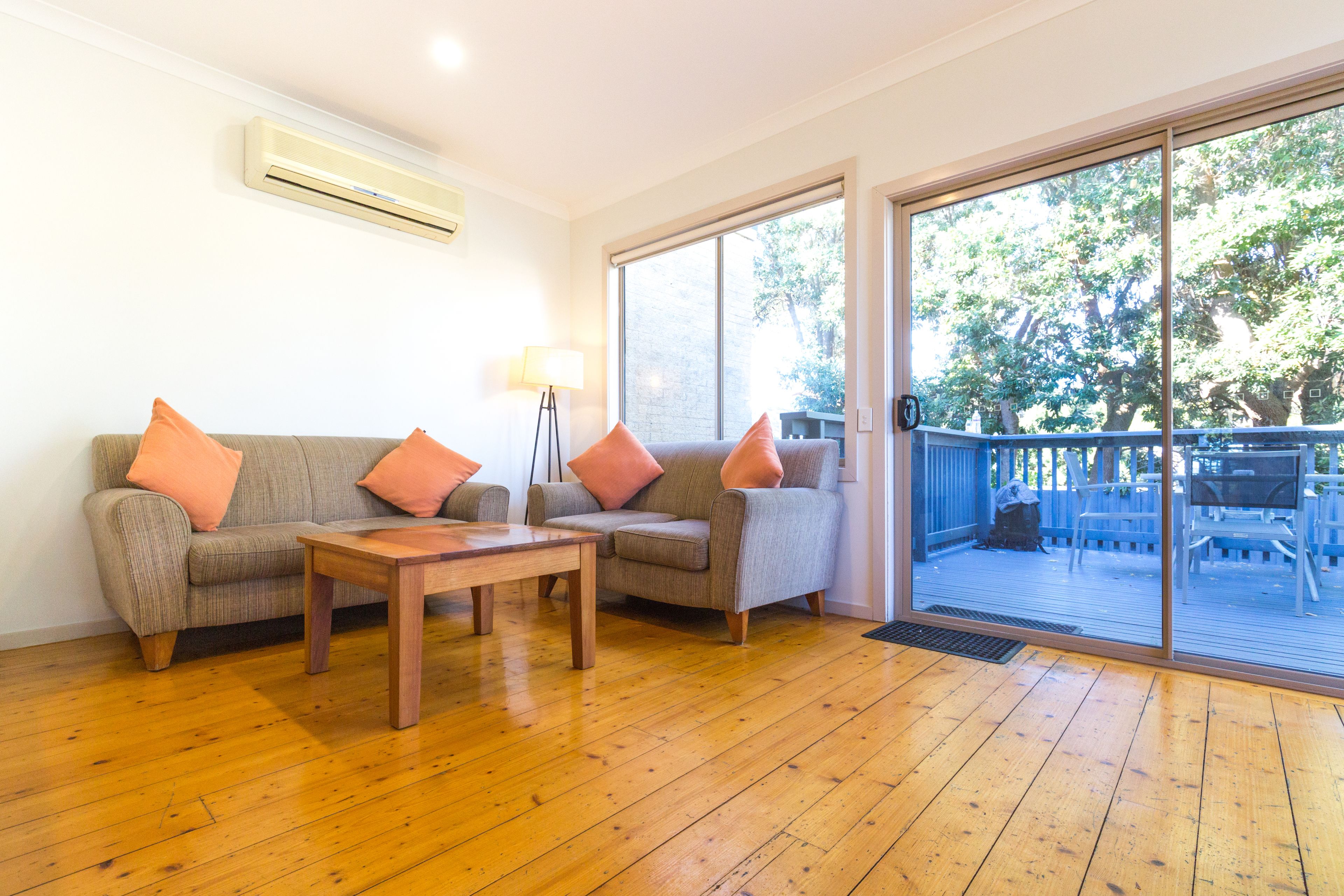 A living room with a sofa set, a coffee table, and a lamp. There is a sliding glass door leading to an outdoor deck.