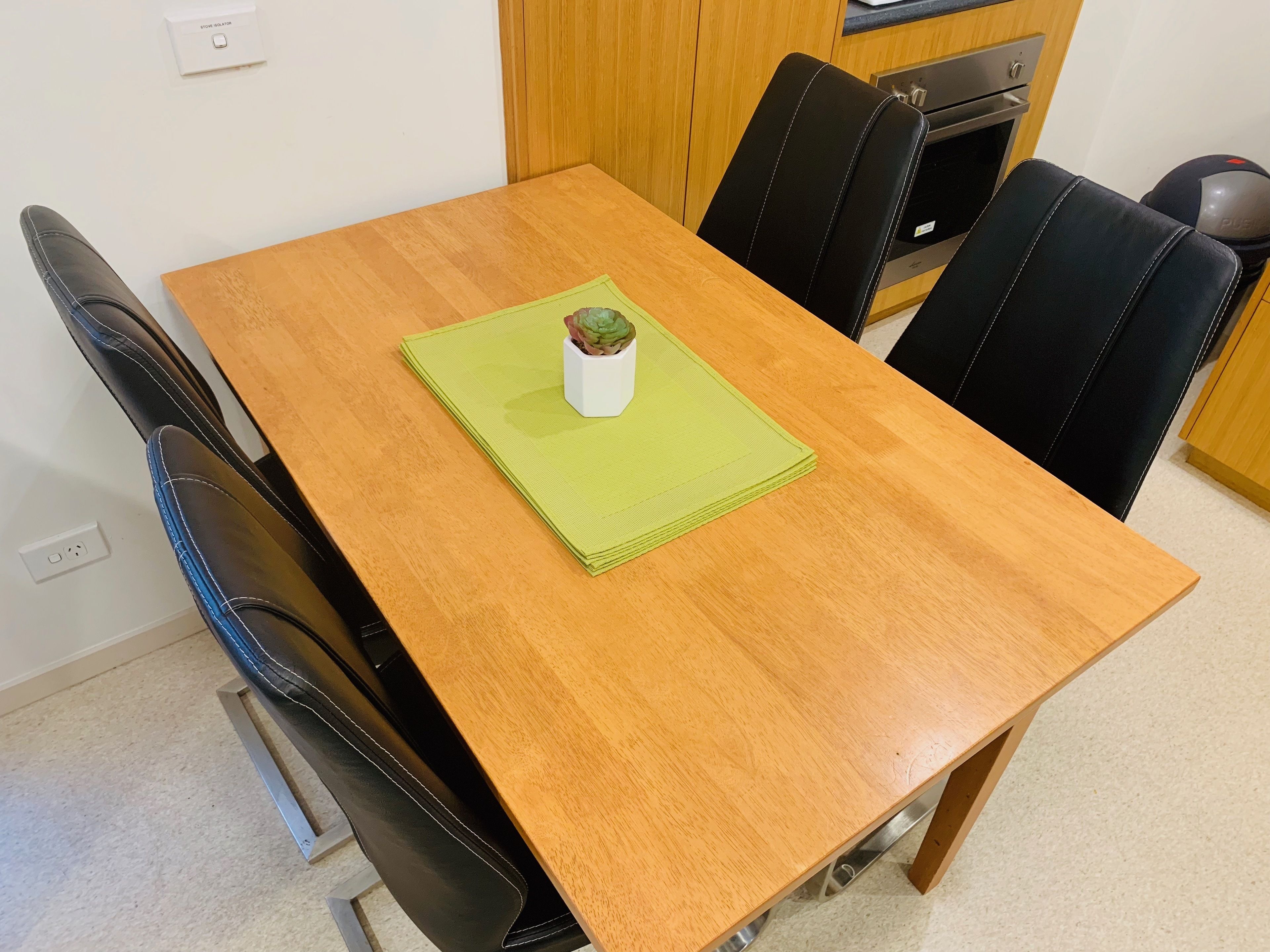 Una mesa de comedor de madera con un mantel individual verde y una pequeña planta en maceta.