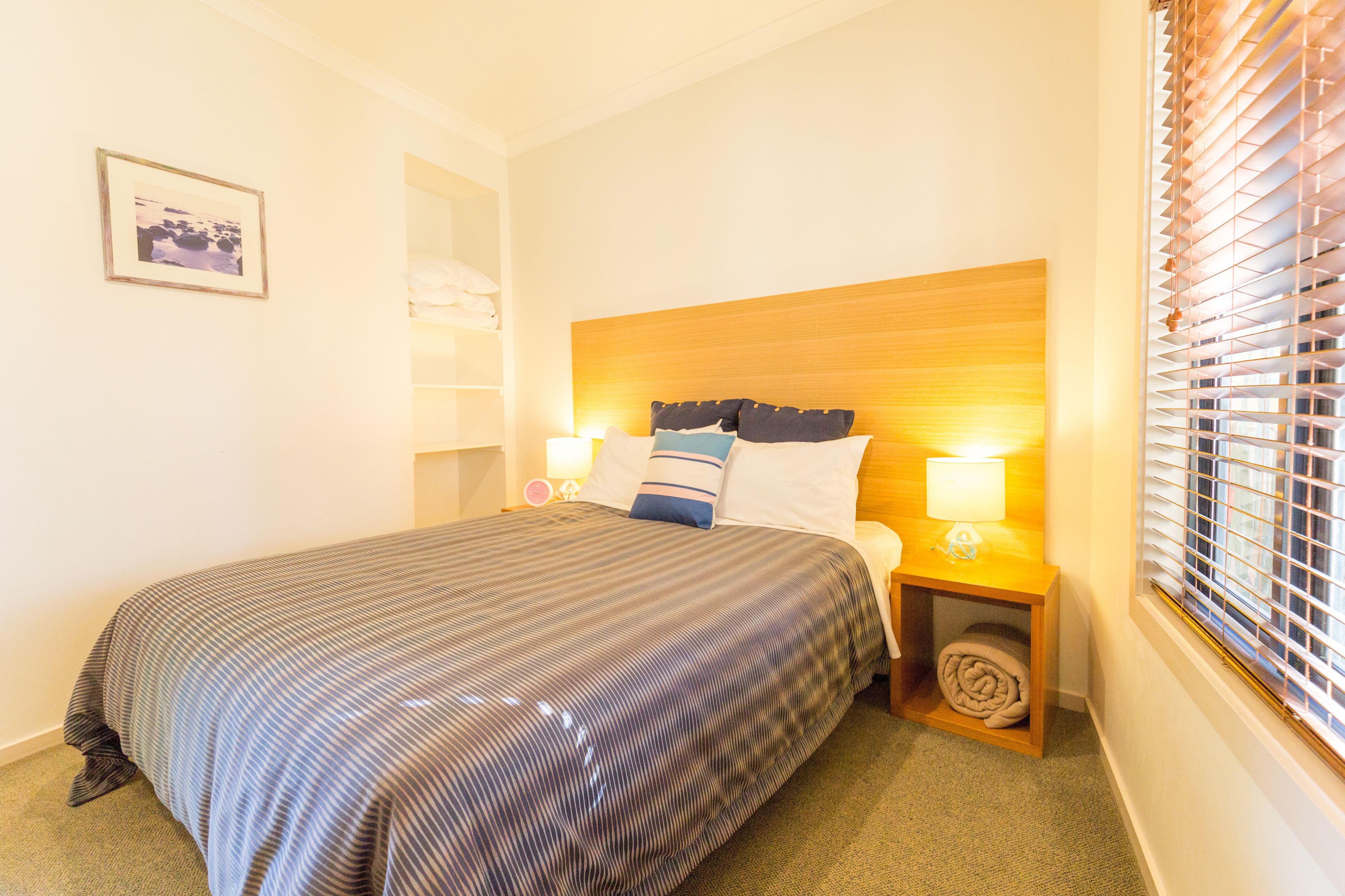 A neatly made bed with a striped bedspread, two bedside lamps, and a wooden headboard.
