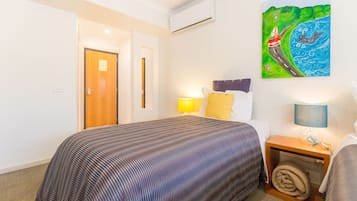 A hotel room with a bed, a nightstand with a lamp, a painting on the wall, and a door leading to another room.