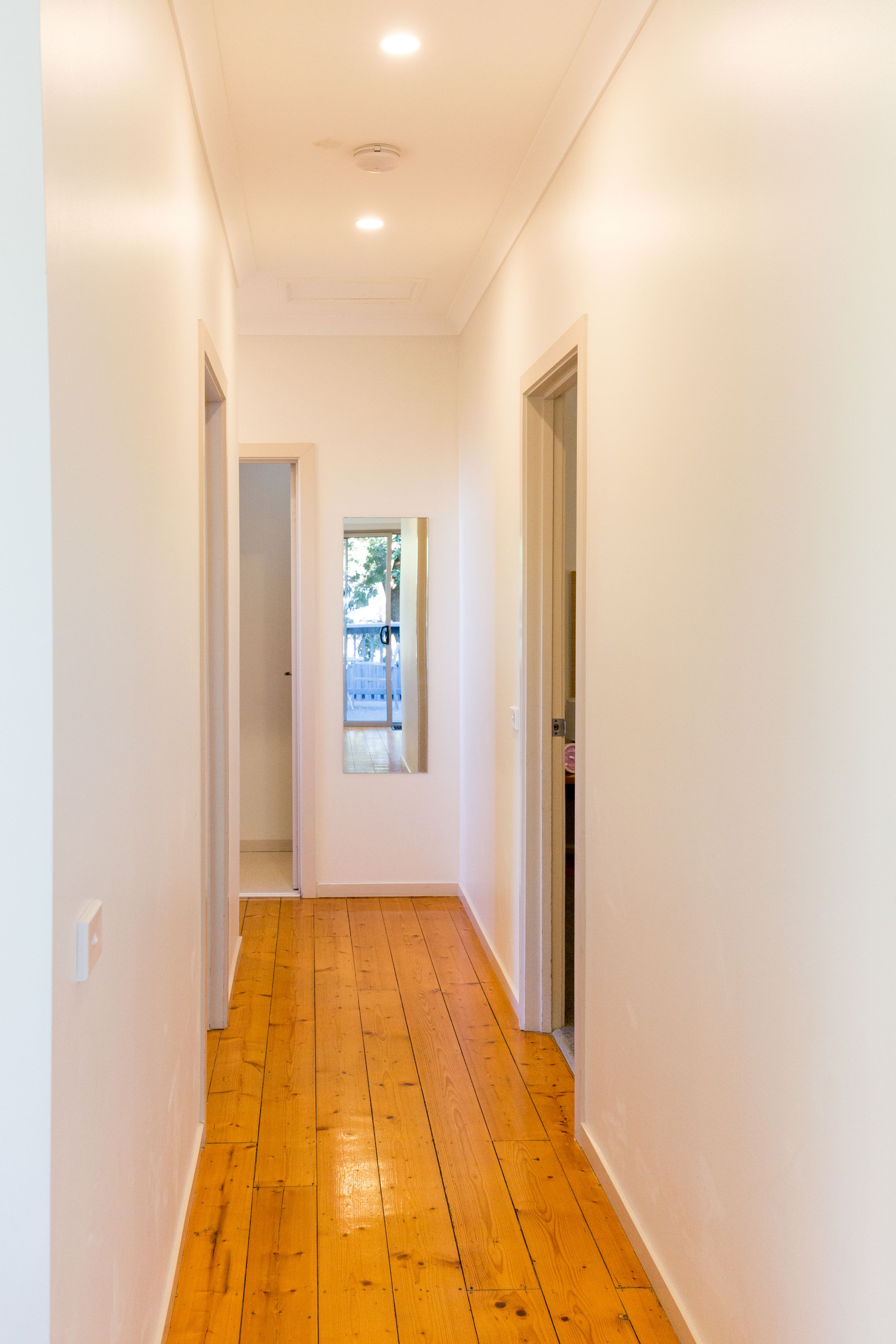 A hallway with wooden flooring and white walls.