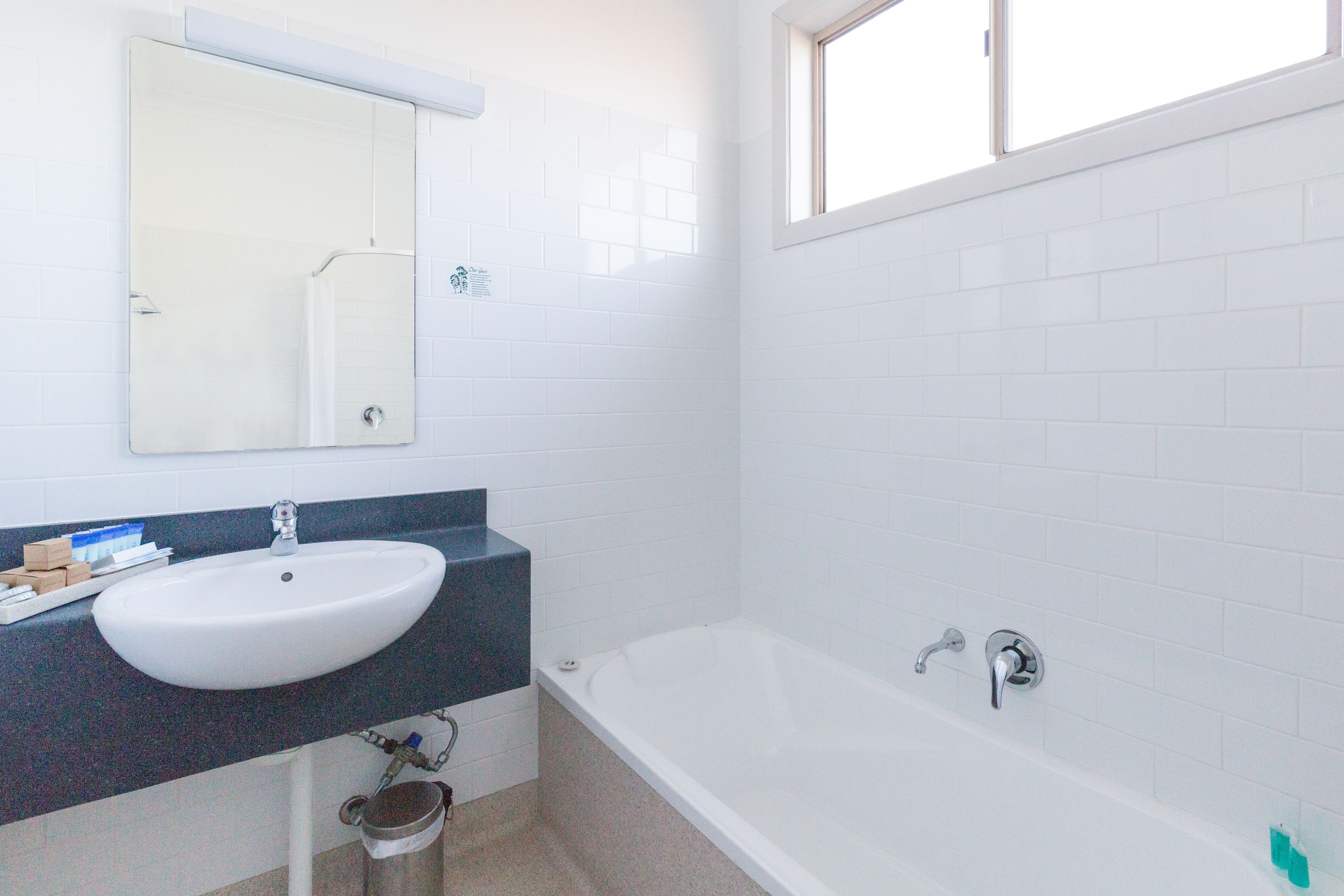 Un baño con lavamanos blanco, espejo, bañera y ventana.