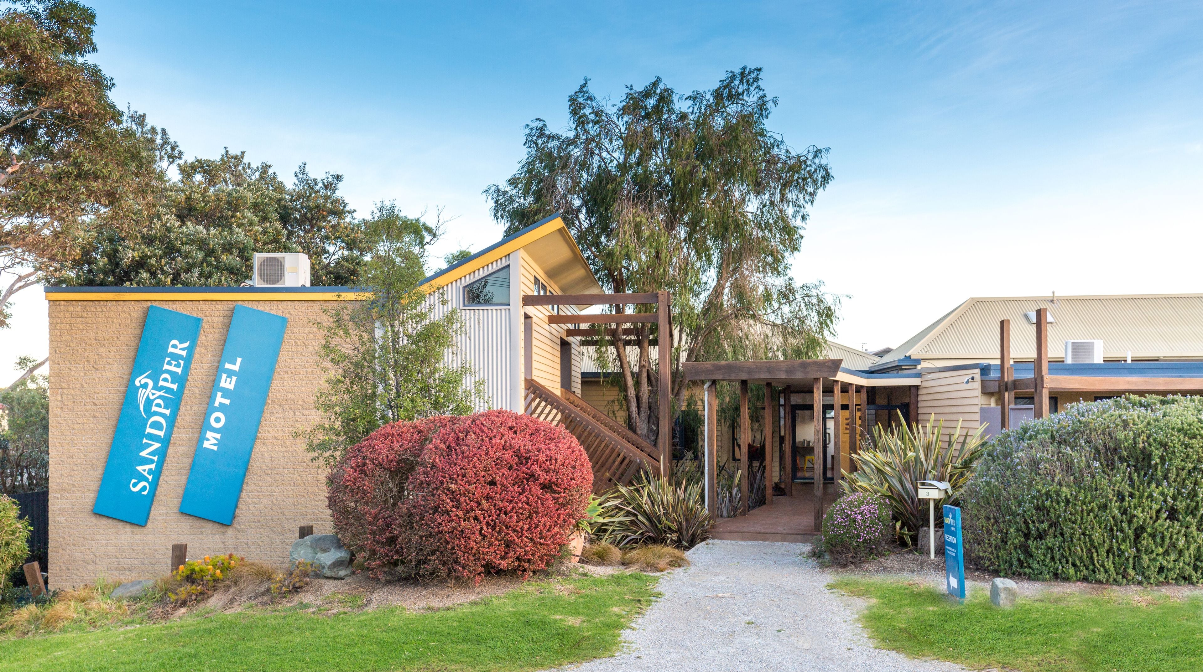 A modern motel with a brick facade, a covered outdoor seating area, and a gravel path leading to the entrance.