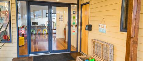 A wooden-floored entrance with a wicker basket filled with toys, a 'Love the Beach' sign, and a no-smoking sign.