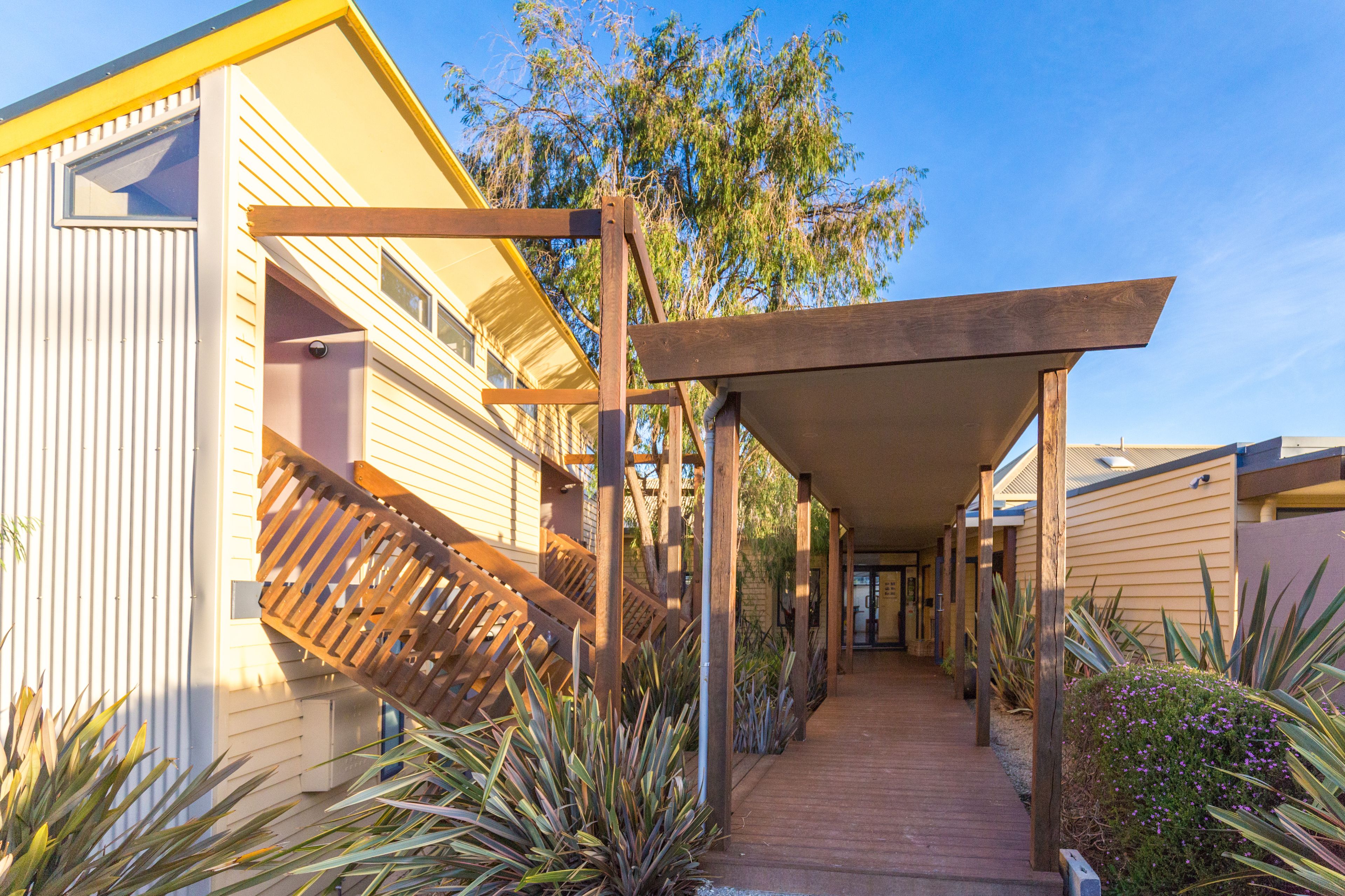 A covered walkway with wooden railings, connecting multiple buildings with a yellow and white exterior.