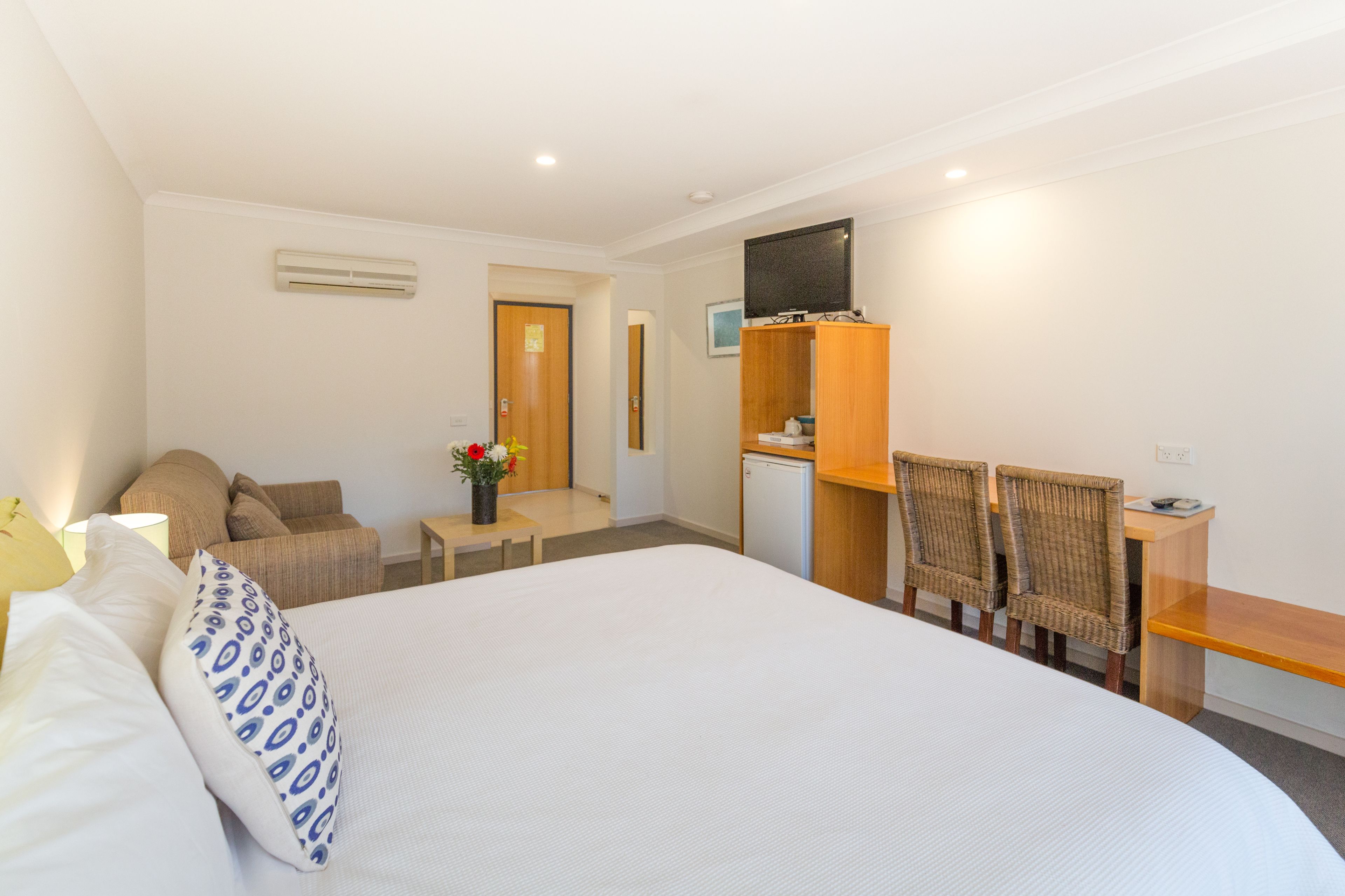 A hotel room with a large bed, a desk with two chairs, a television, and a small kitchenette.
