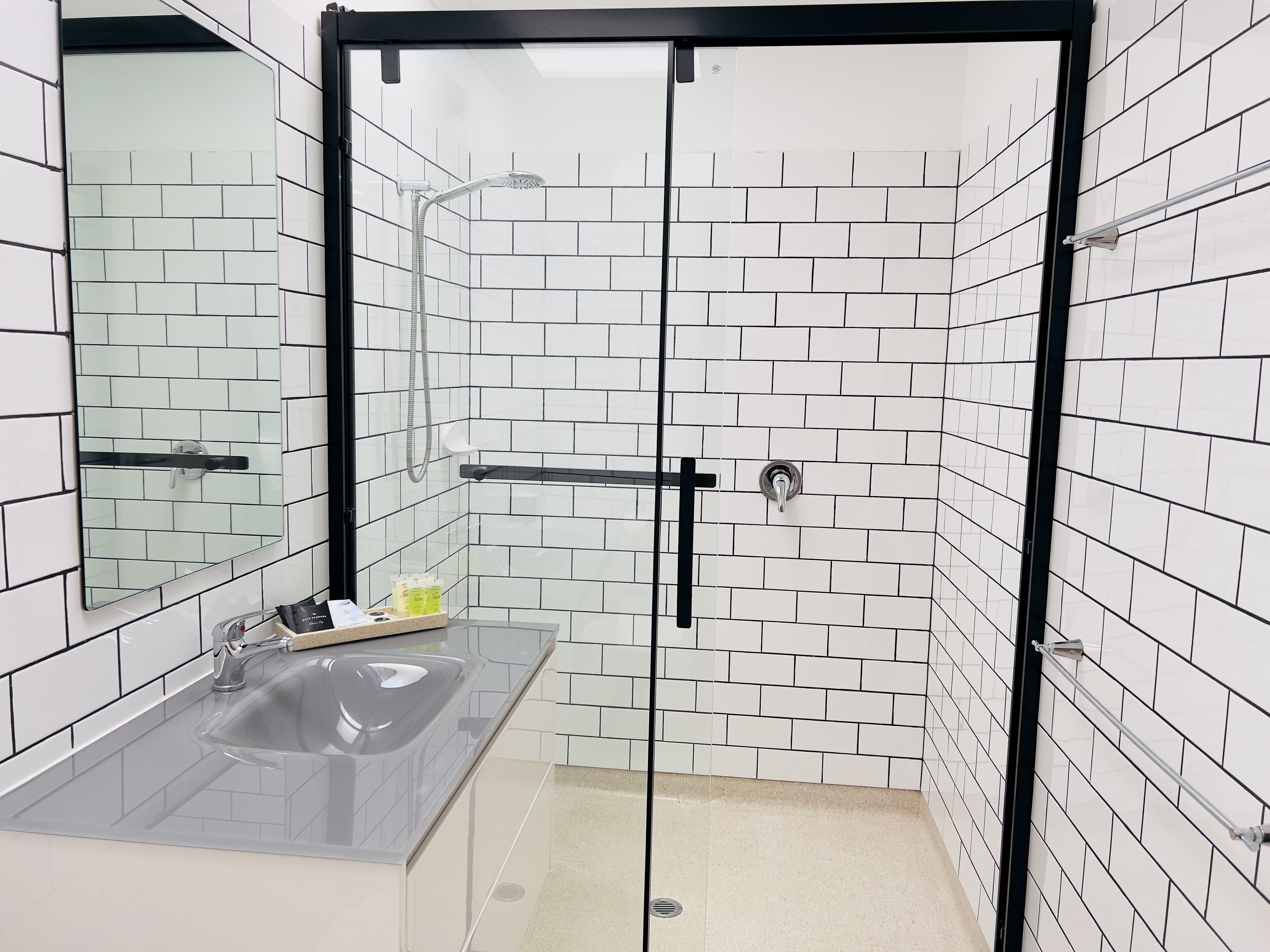 A modern bathroom with white subway tiles, a glass shower enclosure, a sink with a mirror, and a towel rack.