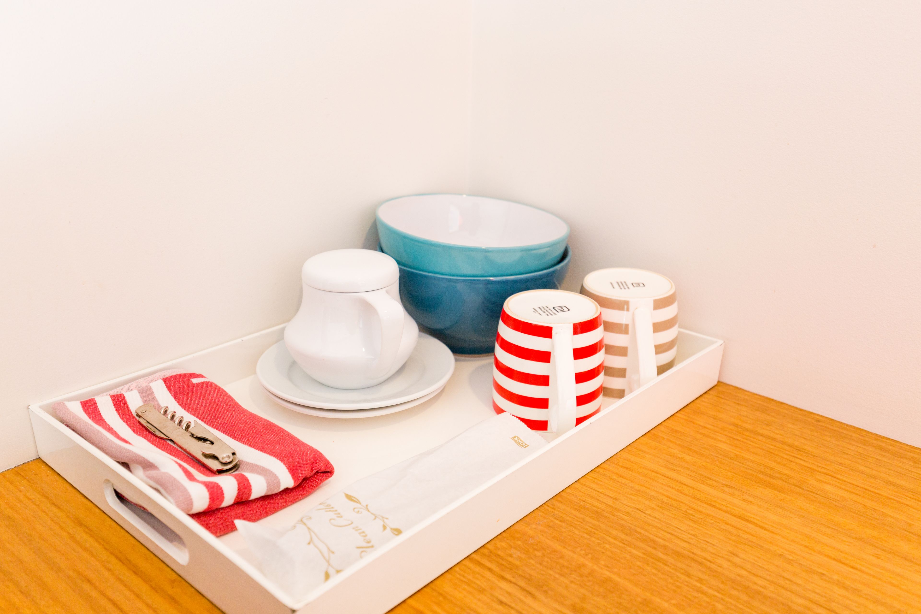 A tray with a white cup, a blue bowl, a striped mug, and a red and white striped towel.