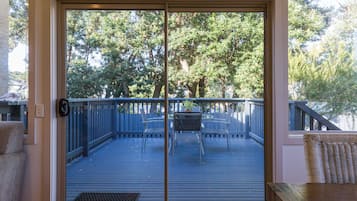 A sliding glass door leading to an outdoor deck with a table and chairs, surrounded by a wooden deck and a blue railing.