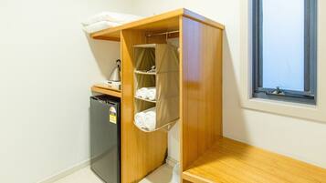 A compact room with a kitchenette, a small refrigerator, a wooden shelf unit with storage, and a window.