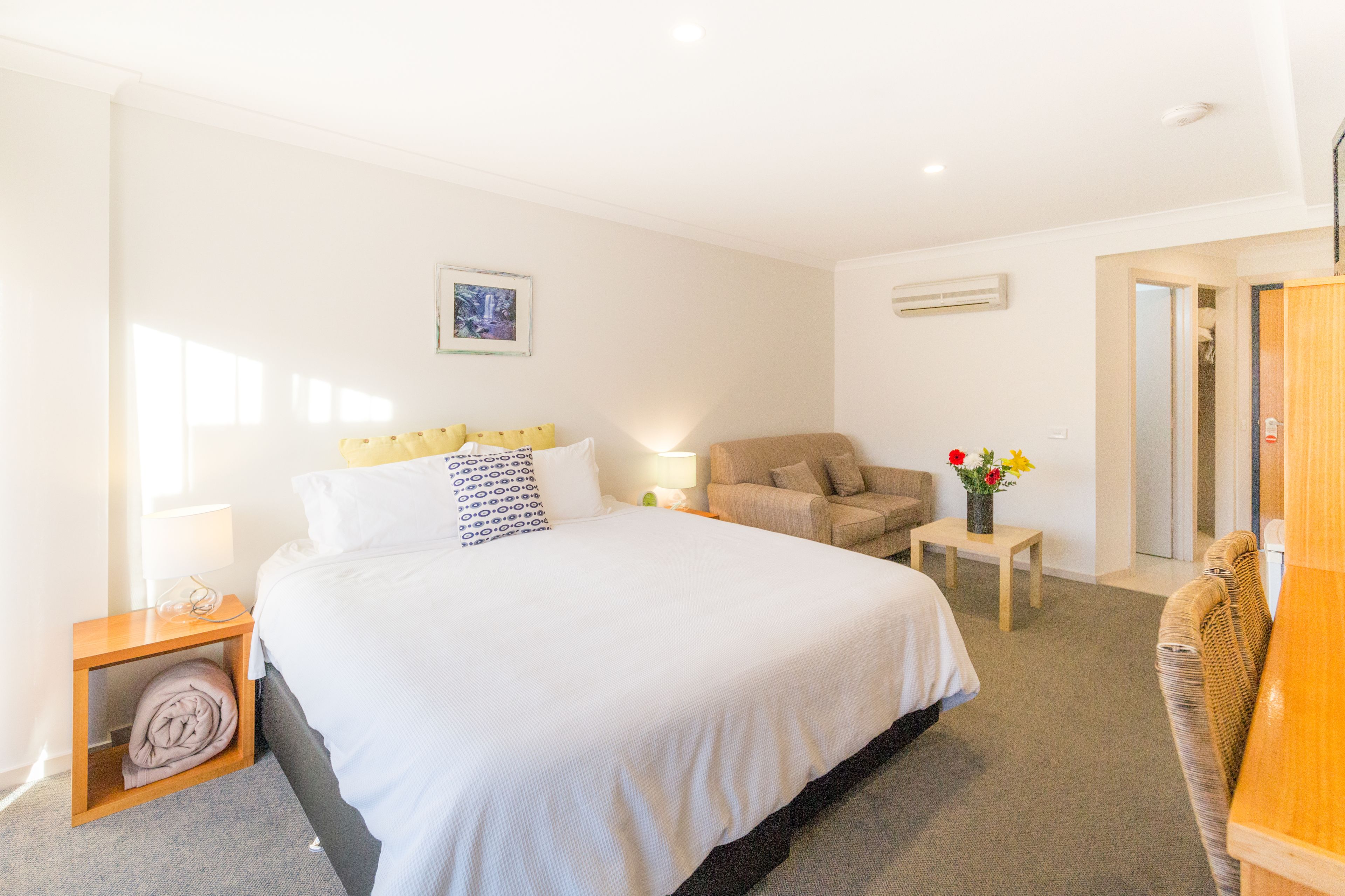 A hotel room with a large bed, a sofa, a small table with a vase of flowers, and a wardrobe.