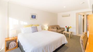A hotel room with a large bed, a sofa, a small table with a vase of flowers, and a wardrobe.
