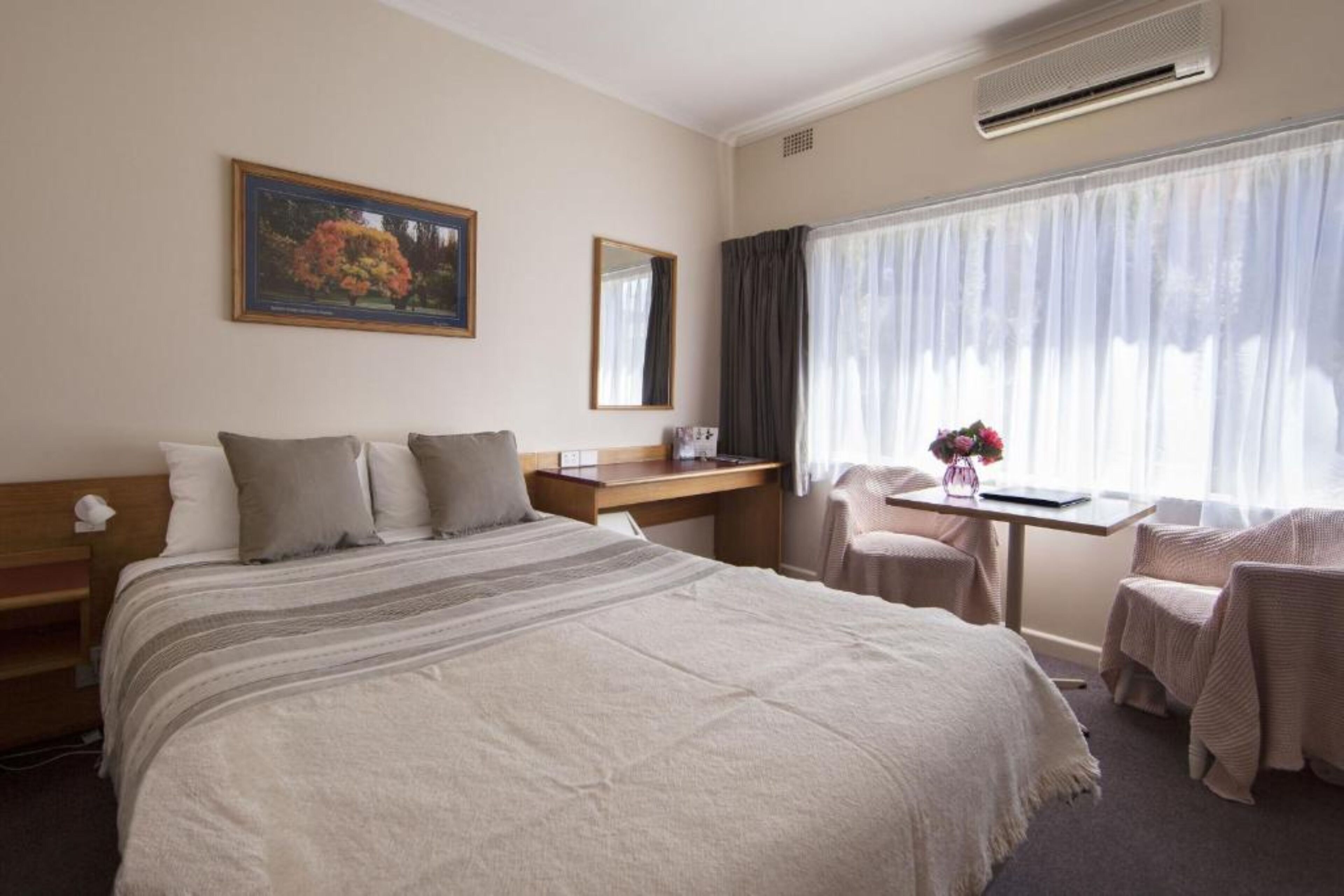 A hotel room with a large bed, a desk, a chair, and a window with curtains.