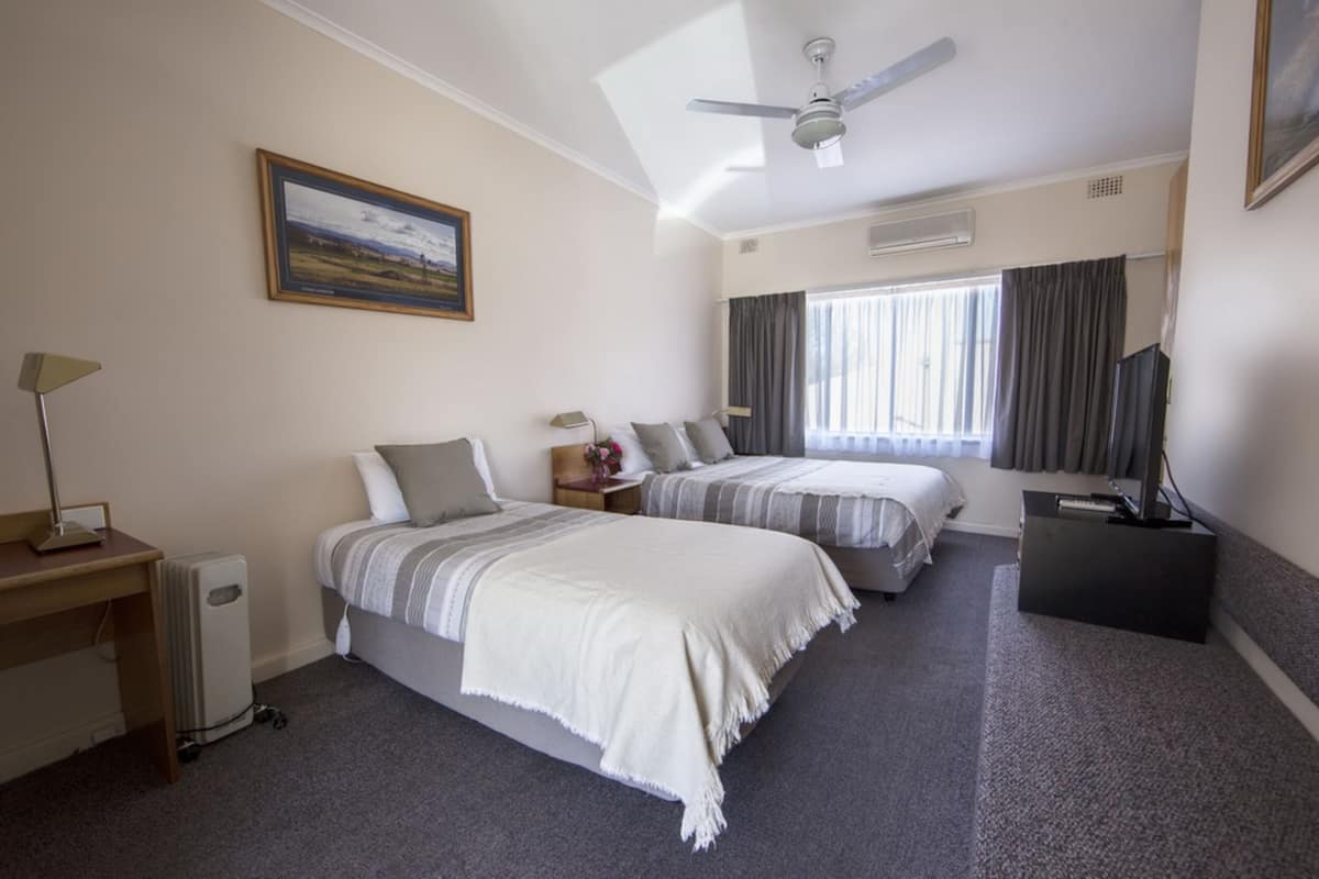 A hotel room with two beds, a desk, a TV, and a ceiling fan.