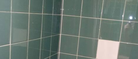 A shower with green tiles and a handheld showerhead.