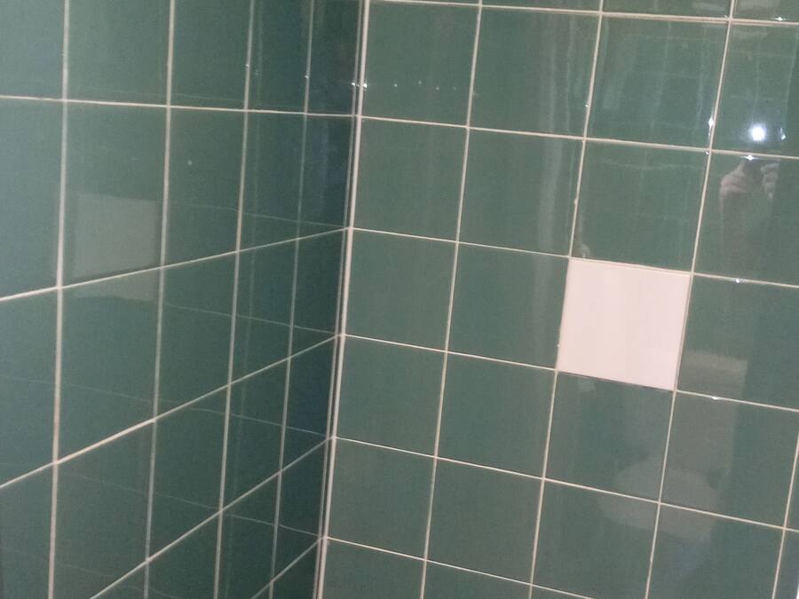 Una ducha con azulejos verdes y un cabezal de ducha de mano.