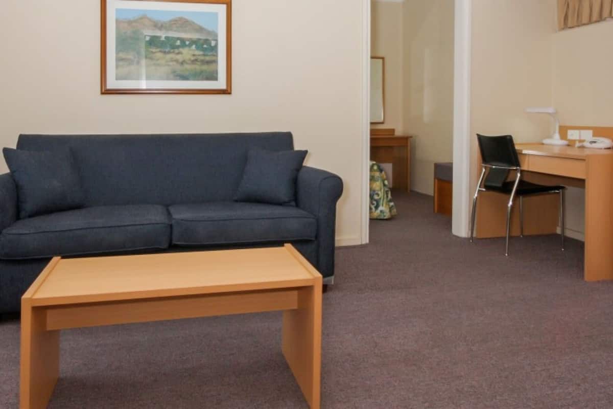 A living room with a sofa, a wooden coffee table, a desk with a chair, and a framed picture on the wall.