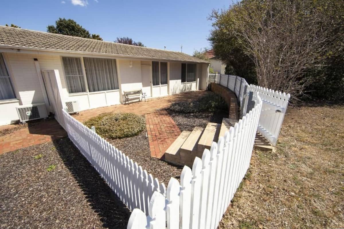 A single-story house with a white exterior, a covered patio, and a white picket fence.