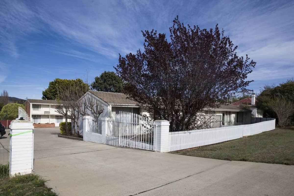 A residential house with a fenced yard, a driveway, and a tree in front.