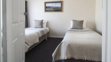 A room with two single beds, a framed landscape painting on the wall, and a door leading to another room.