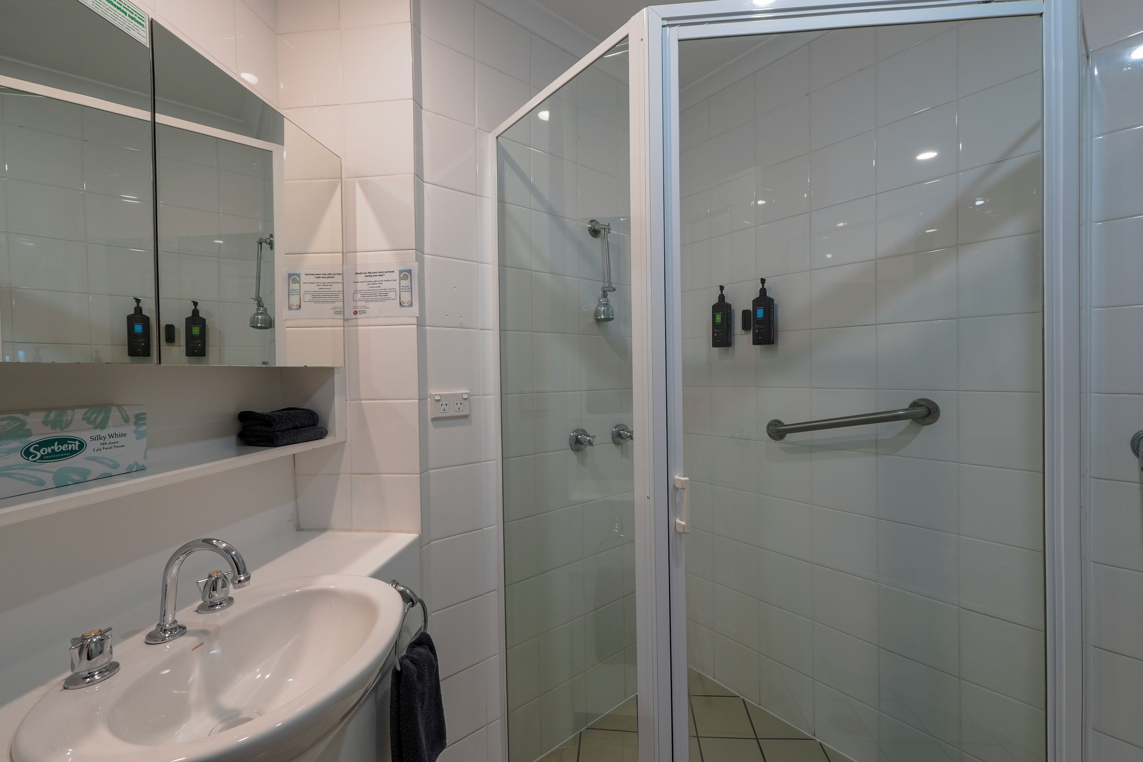 Ein modernes Badezimmer mit einer gläsernen Duschkabine, einem Waschbecken mit Spiegel und Pflegeprodukten an der Wand.