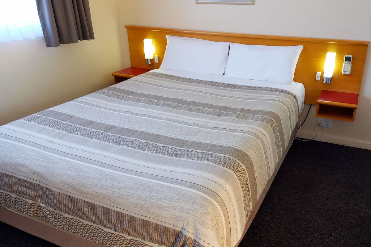 A neatly made bed with a striped bedspread, two bedside tables with lamps, and a power outlet on the wall.