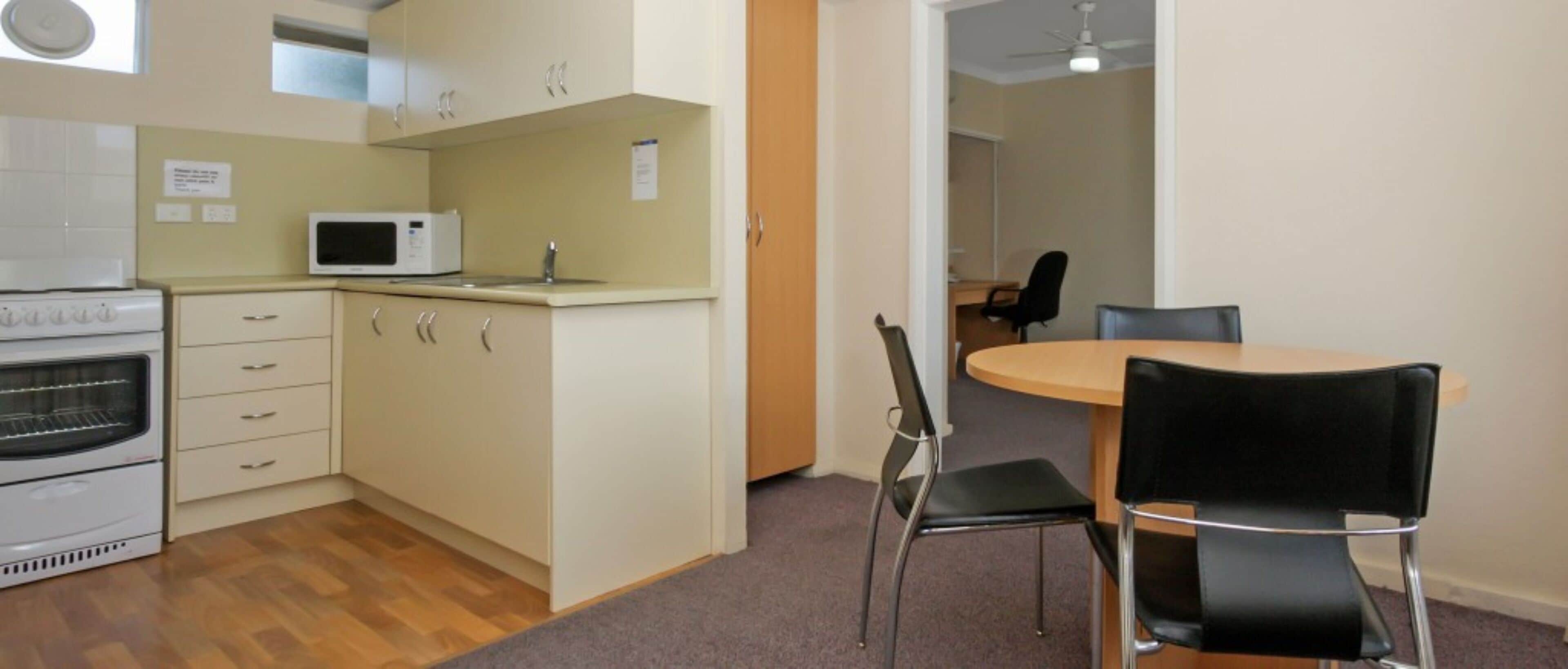 A compact kitchen with a microwave, oven, and cabinets. There is a dining area with a table and chairs.