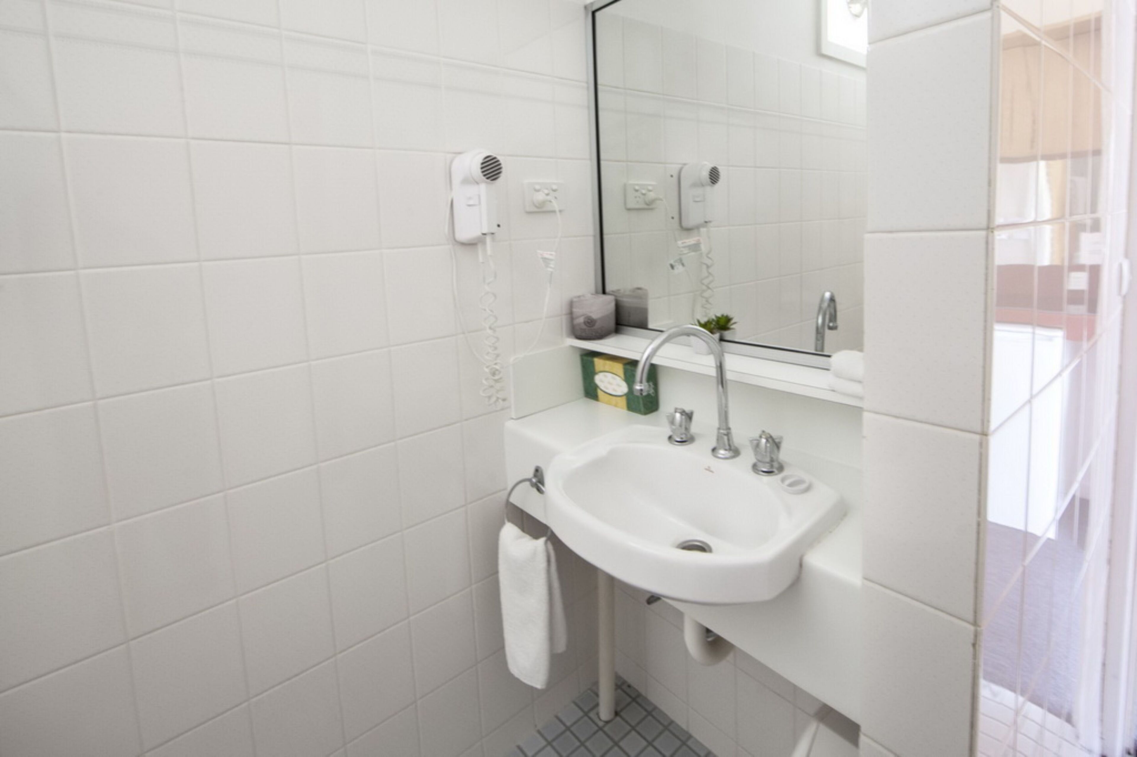 Casa de banho moderna com azulejos brancos, uma sanita branca, um espelho, um secador de cabelo e um porta-toalhas.