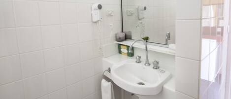 A modern bathroom with white tiles, a white sink, a mirror, a hairdryer, and a towel rack.