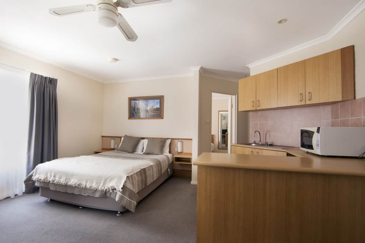 A hotel room with a bed, a desk, a microwave, and a ceiling fan.