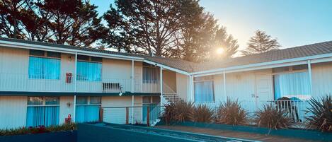 A two-story motel with a brick facade, numbered rooms, and a small outdoor area with plants.