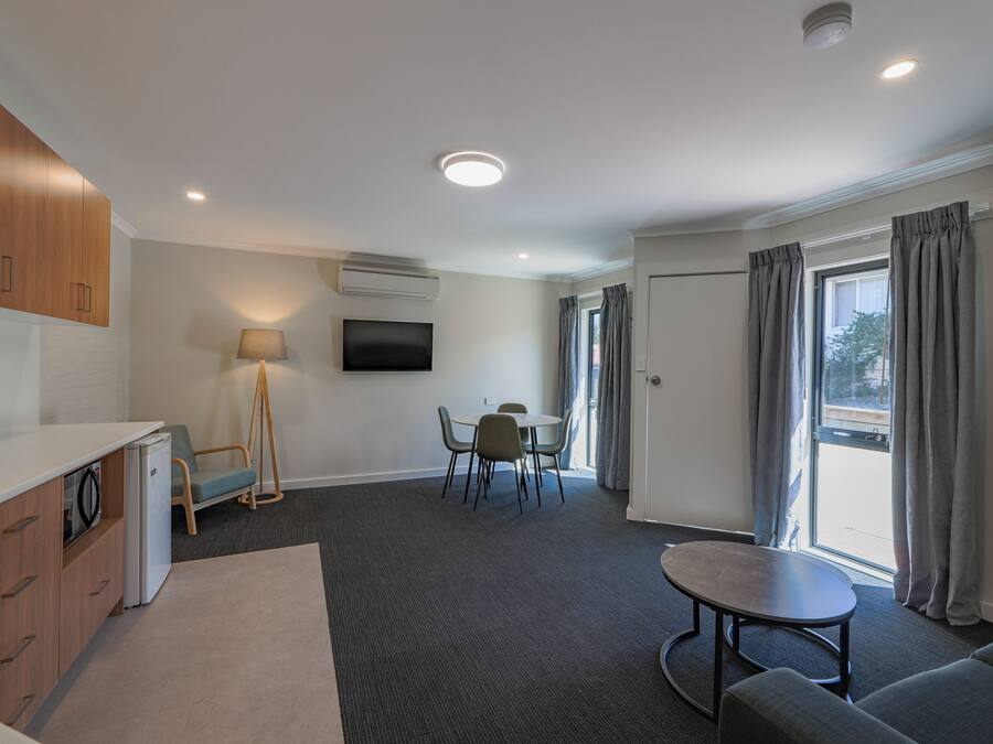 Quarto de hotel moderno com cozinha compacta, área de refeições, sofá e uma grande janela com cortinas.