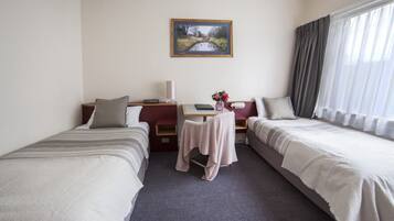 Habitación de hotel con dos camas individuales, una mesita con lámpara, un cuadro en la pared y una ventana con cortinas.