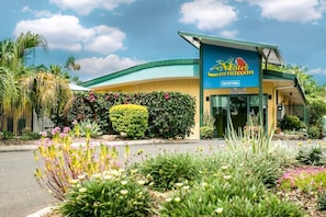 Un motel con área de recepción, techo curvo y un jardín bien cuidado con diversas plantas y flores.